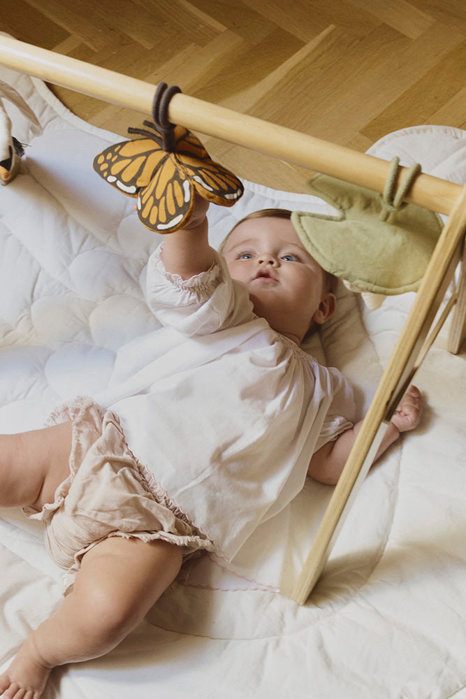 Baby playing with a butterfly toy hanging from wooden play gym