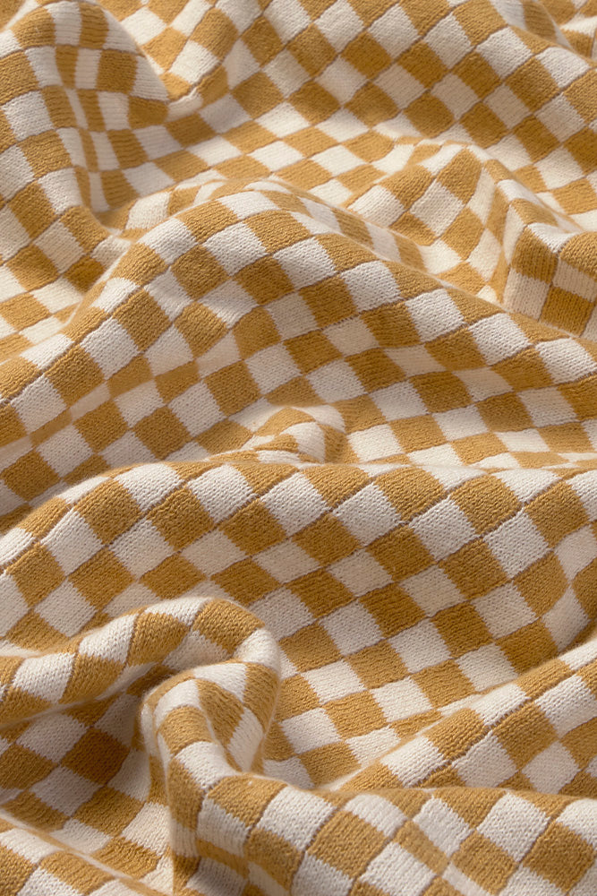 Close-up of a checkered throw blanket with honey yellow and white squares.