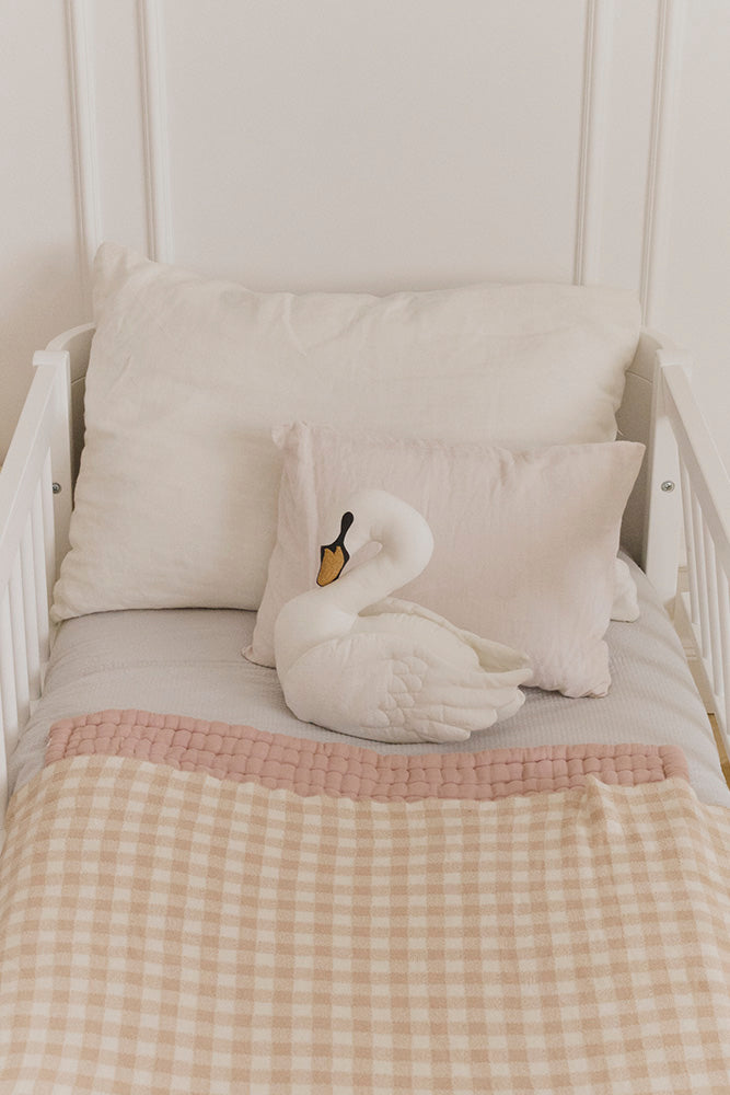 White swan throw pillow on a bed with checkered rose blanket and pillows.