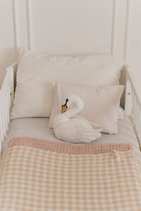 White swan throw pillow on a bed with checkered rose blanket and pillows.