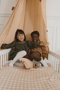 Two children sitting on a bed with a rose checkered blanket