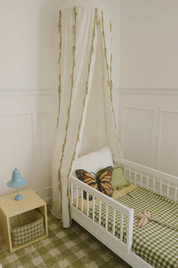 Children's room with a white toddler bed, green checkered blanket and rug, and decorative butterfly pillow.