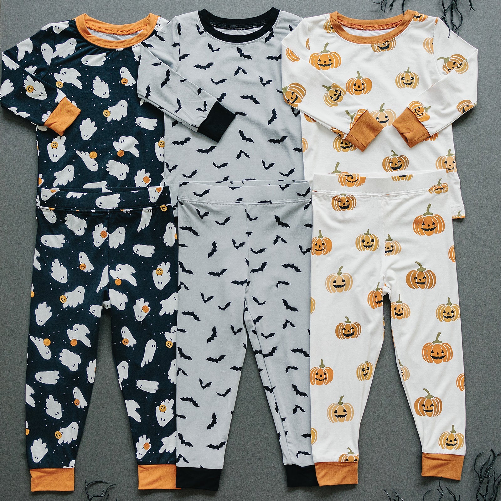 Three Halloween-themed children's pajama sets on a gray background.