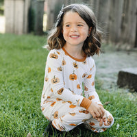 Child wearing a Halloween-themed onesie with pumpkins sitting on grass.