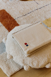 Round natural floor cushion edged with pom-poms
