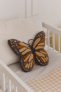 Butterfly-shaped pillow on a white toddler bed with checkered blanket
