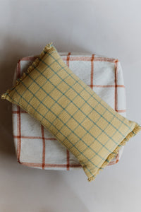 Yellow checkered fringed pillow on top of grid line pouf