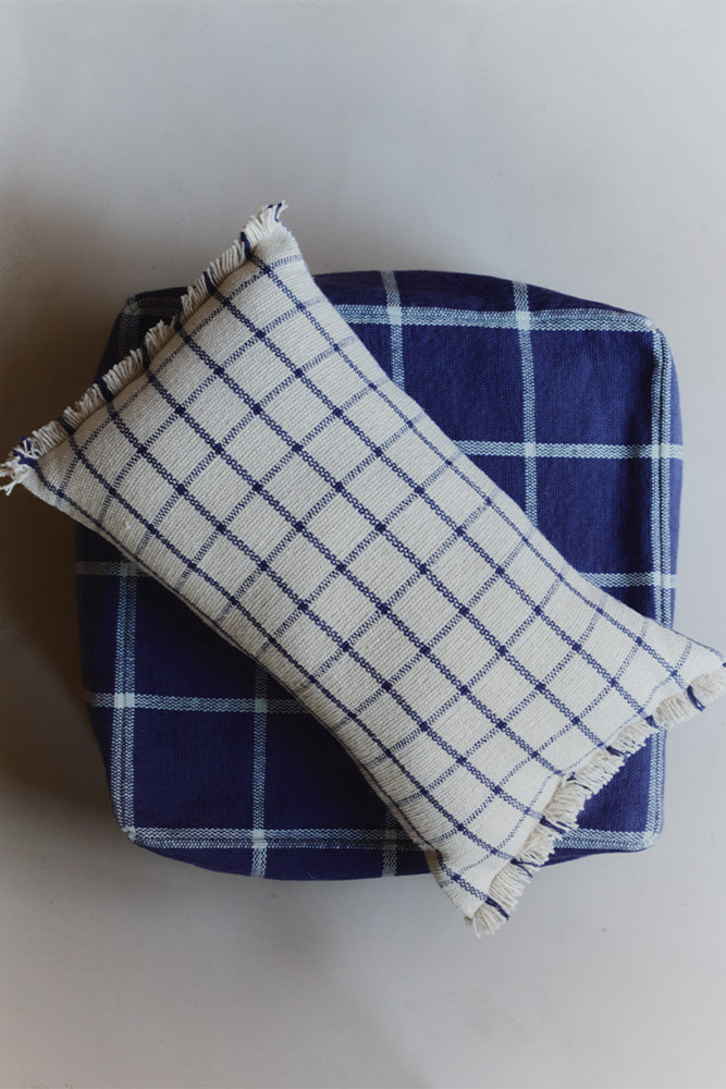 Natural checked pillow with navy gridlines on top of navy pouf