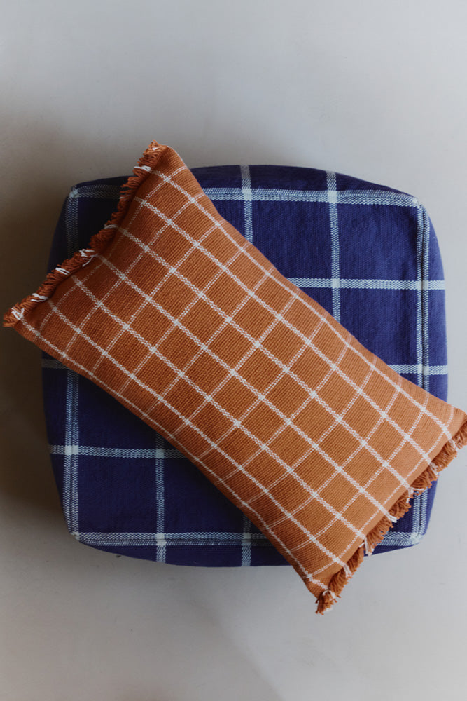 Terracotta checked throw pillow on top of navy pouf