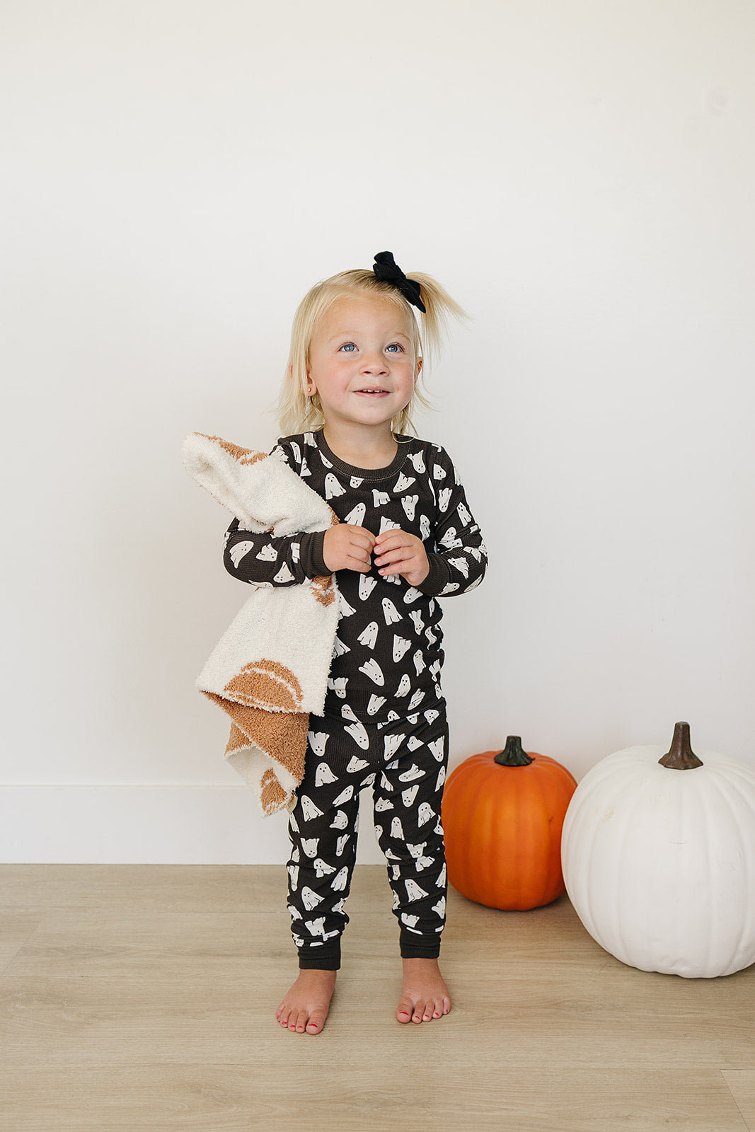 Child wearing a black and white patterned Halloween ghost pajamas with pumpkins in the background