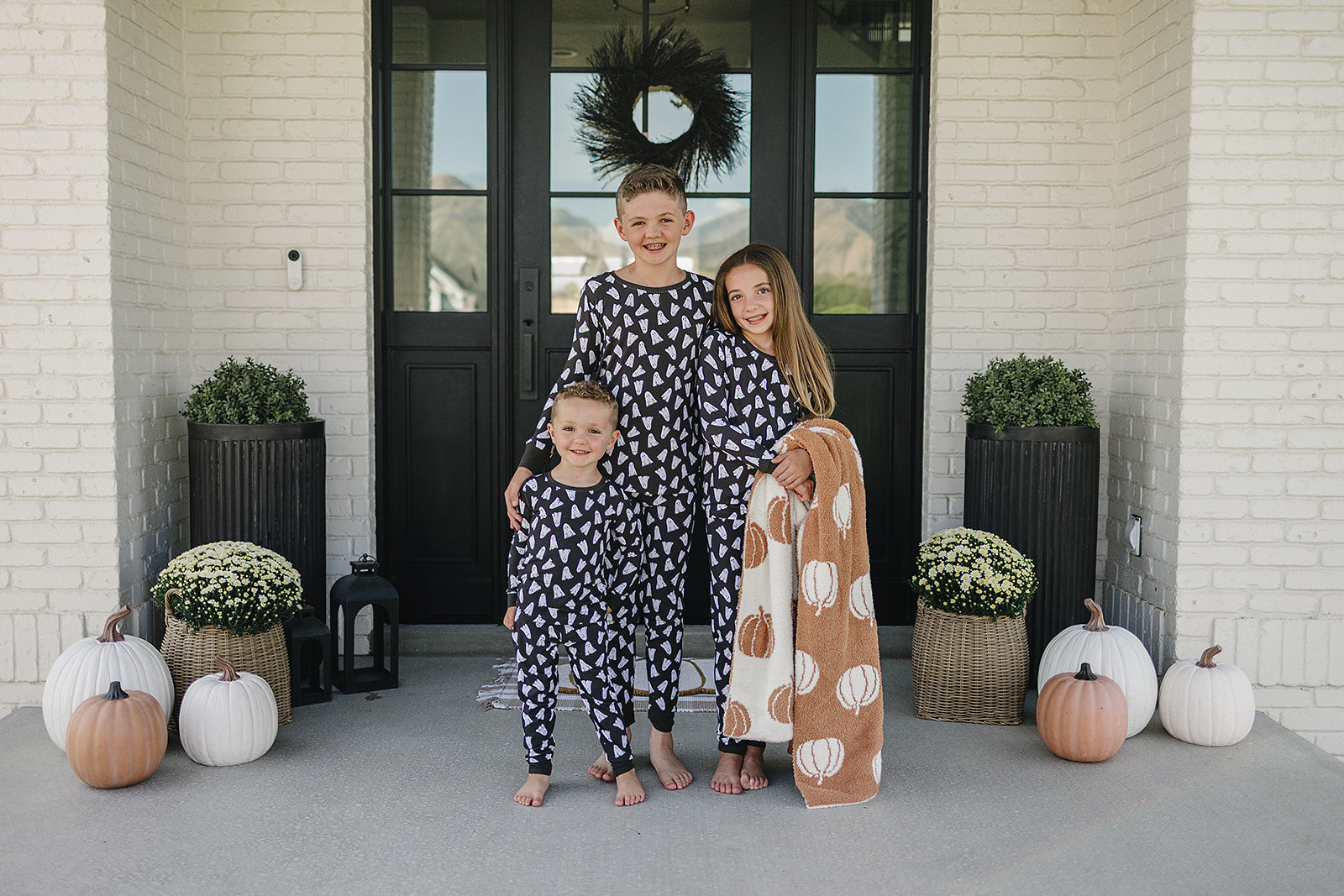 Family in matching Halloween ghost pajamas standing on a porch with Halloween decorations.