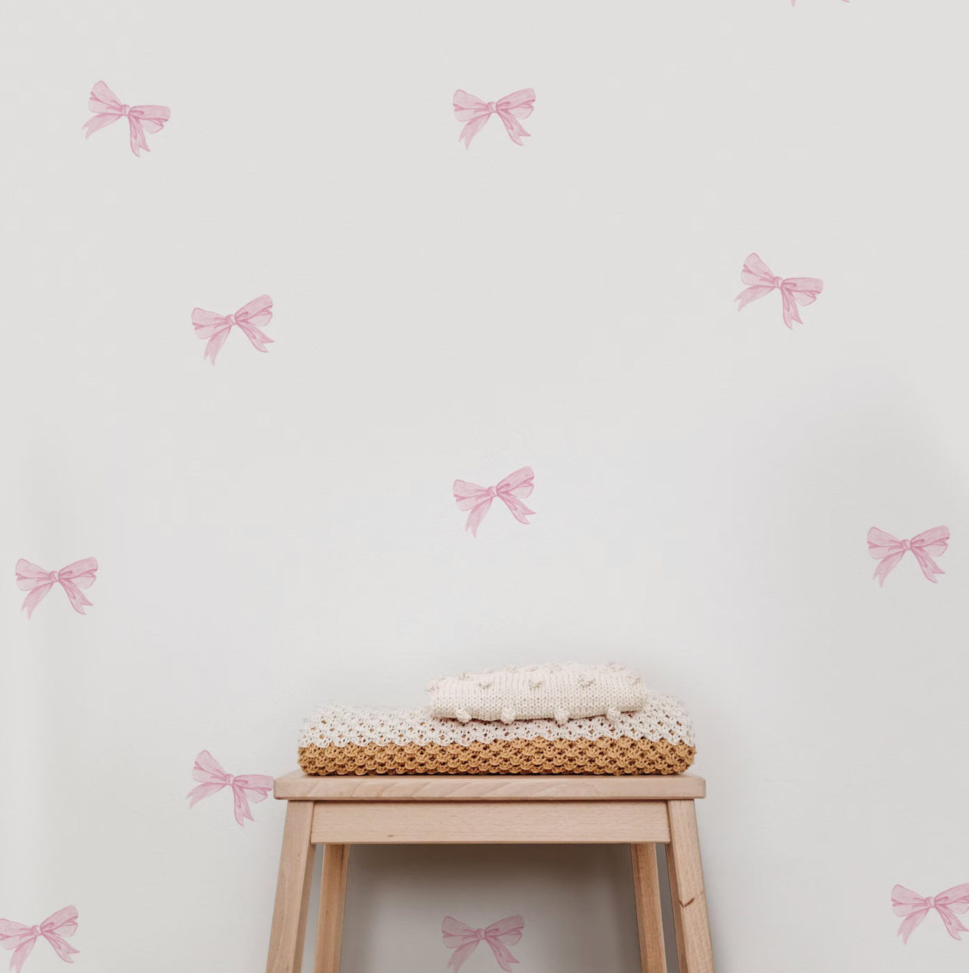A room with pink bow wall decals stickers, featuring a wooden stool with a basket on it in the foreground.
