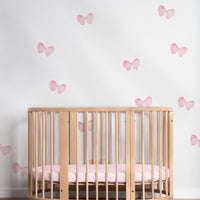 Pink coquette bow wall decals around a wooden crib in a nursery room.