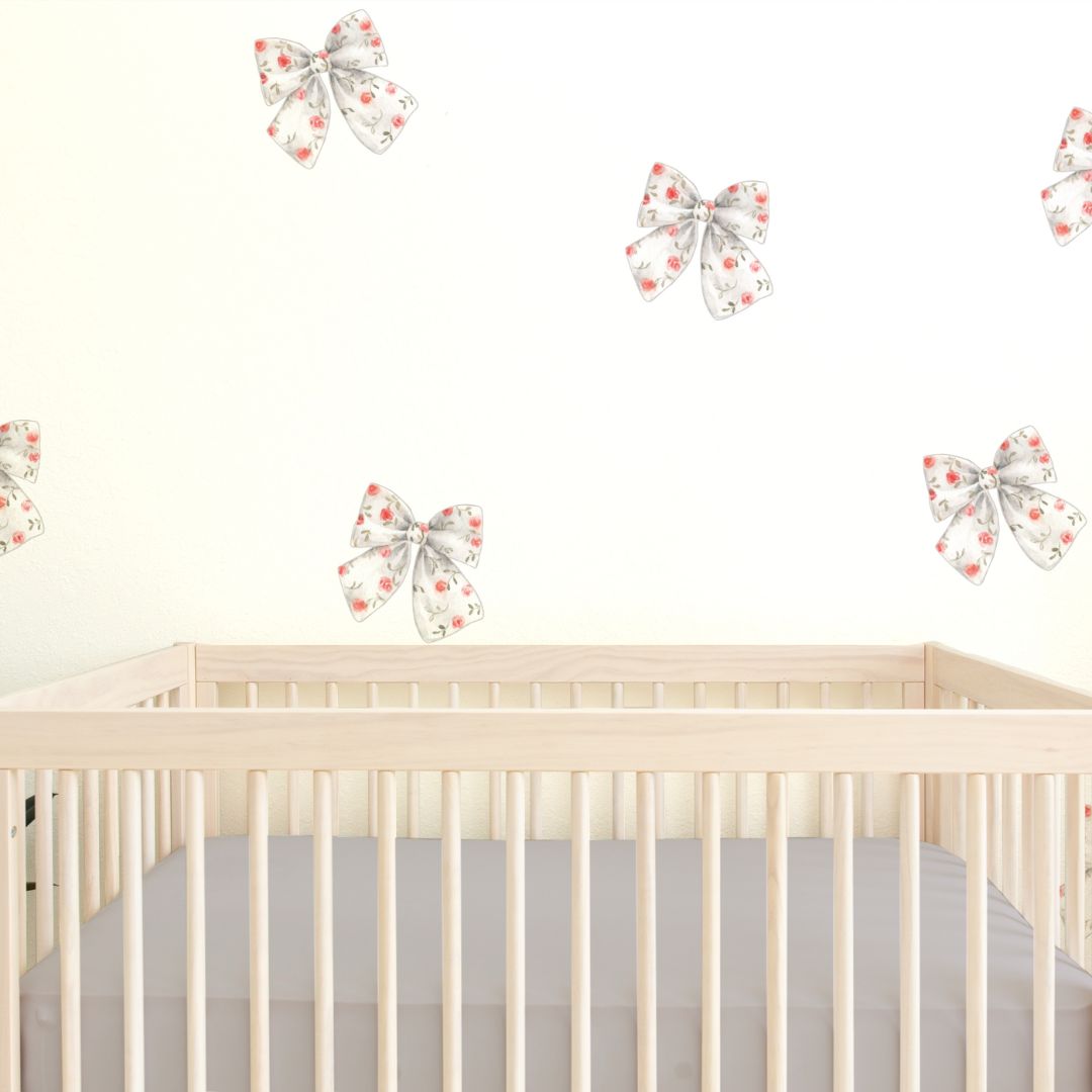 A nursery with white walls featuring a set of rosy bow wall decal stickers above a beige crib, with a focus on the wall decals.