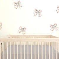 A nursery with white walls featuring a set of rosy bow wall decal stickers above a beige crib, with a focus on the wall decals.