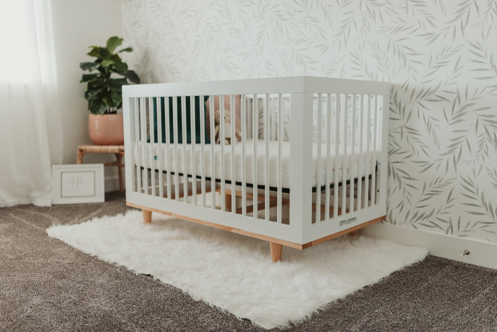 Light Green Botanical Foliage Wallpaper in the background with a crib in the foreground - Project Nursery