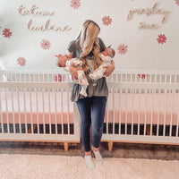 mom holding twins in a nursery with pink daisy floral wall decals background